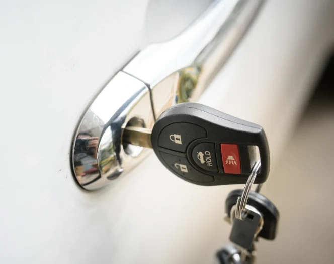 A close-up of a black car key with remote buttons inserted into a chrome handle lock on a white car door.